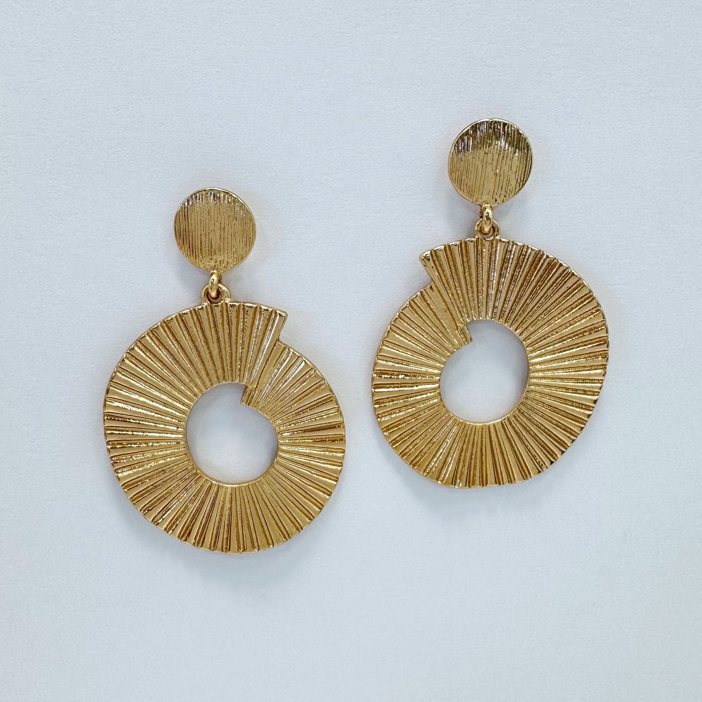 A pair of gold-colored drop dangle earrings with a textured surface, displayed against a white background.