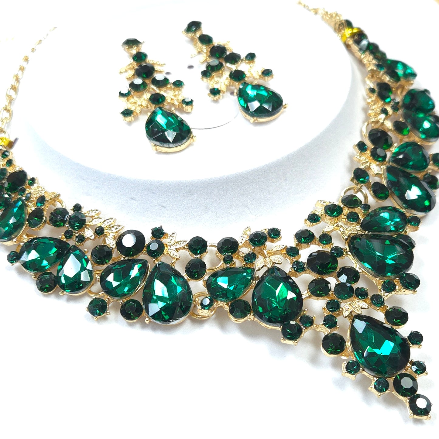 Jewelry set with emerald green stones and gold accents on a white background