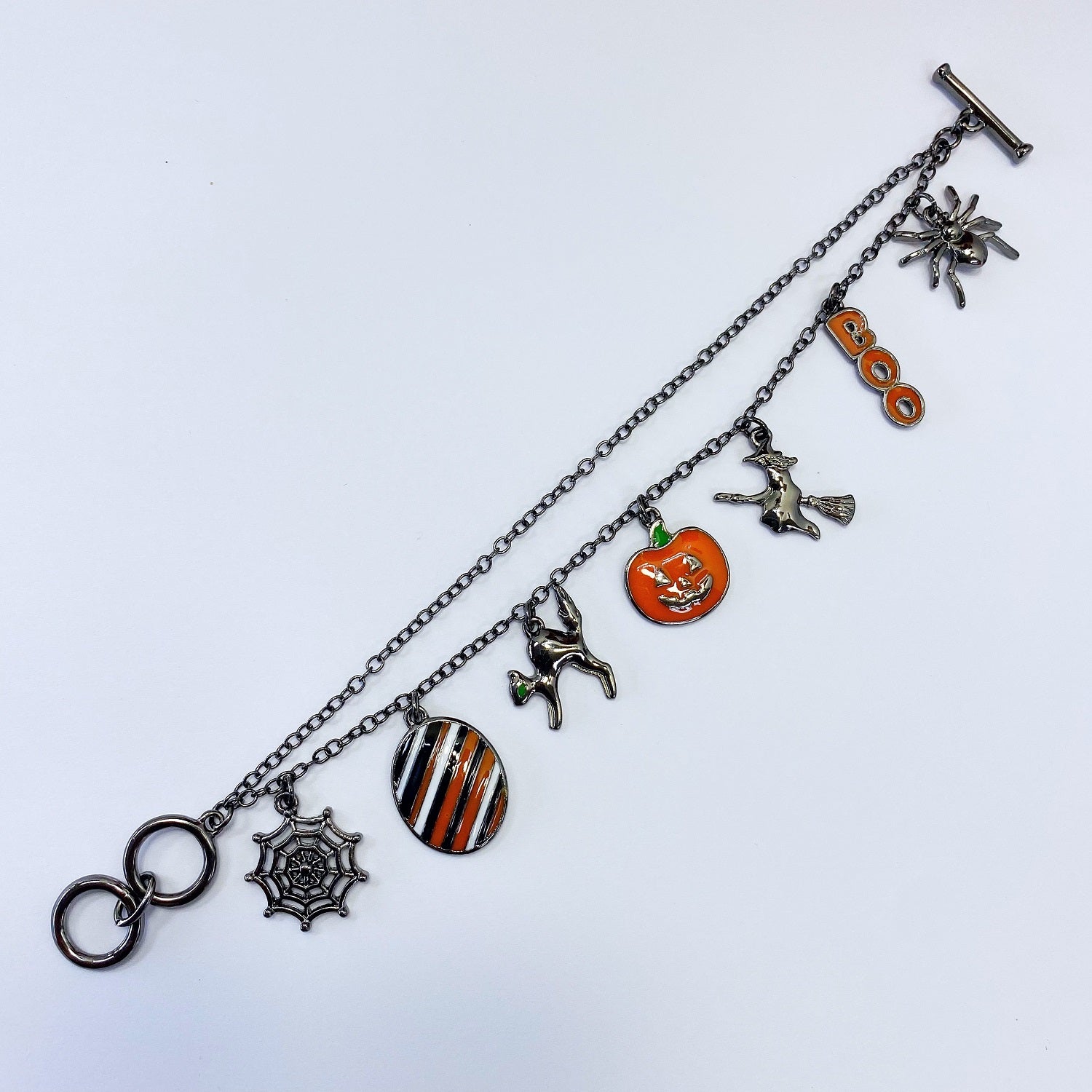 Halloween charm bracelet featuring pumpkin, witch, spiderweb, ghost, and striped enamel charms on a chain link bracelet.