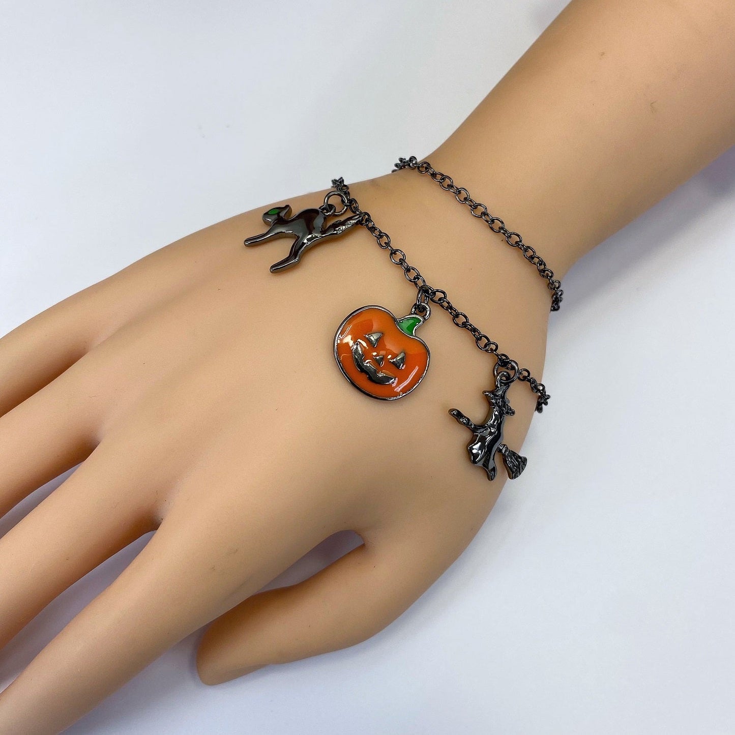 Halloween charm bracelet featuring pumpkin, witch, spiderweb, ghost, and striped enamel charms on a chain link bracelet.