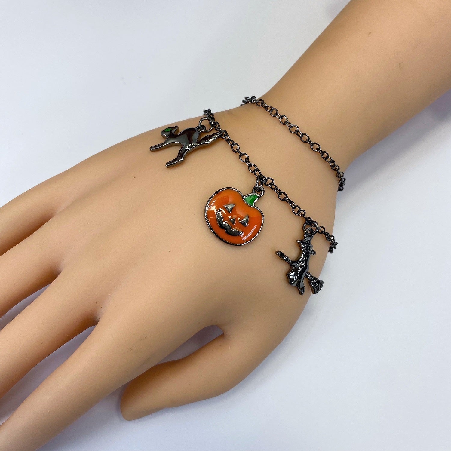 Halloween charm bracelet featuring pumpkin, witch, spiderweb, ghost, and striped enamel charms on a chain link bracelet.