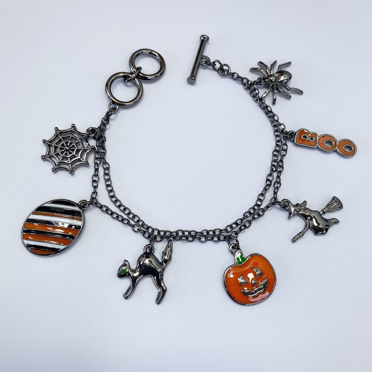 Halloween charm bracelet featuring pumpkin, witch, spiderweb, ghost, and striped enamel charms on a chain link bracelet.