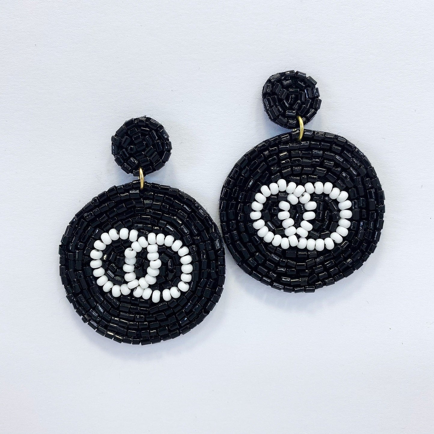 A pair of black and white circle-shaped bead earrings with a dangle post and drop design, displayed on a mannequin head.