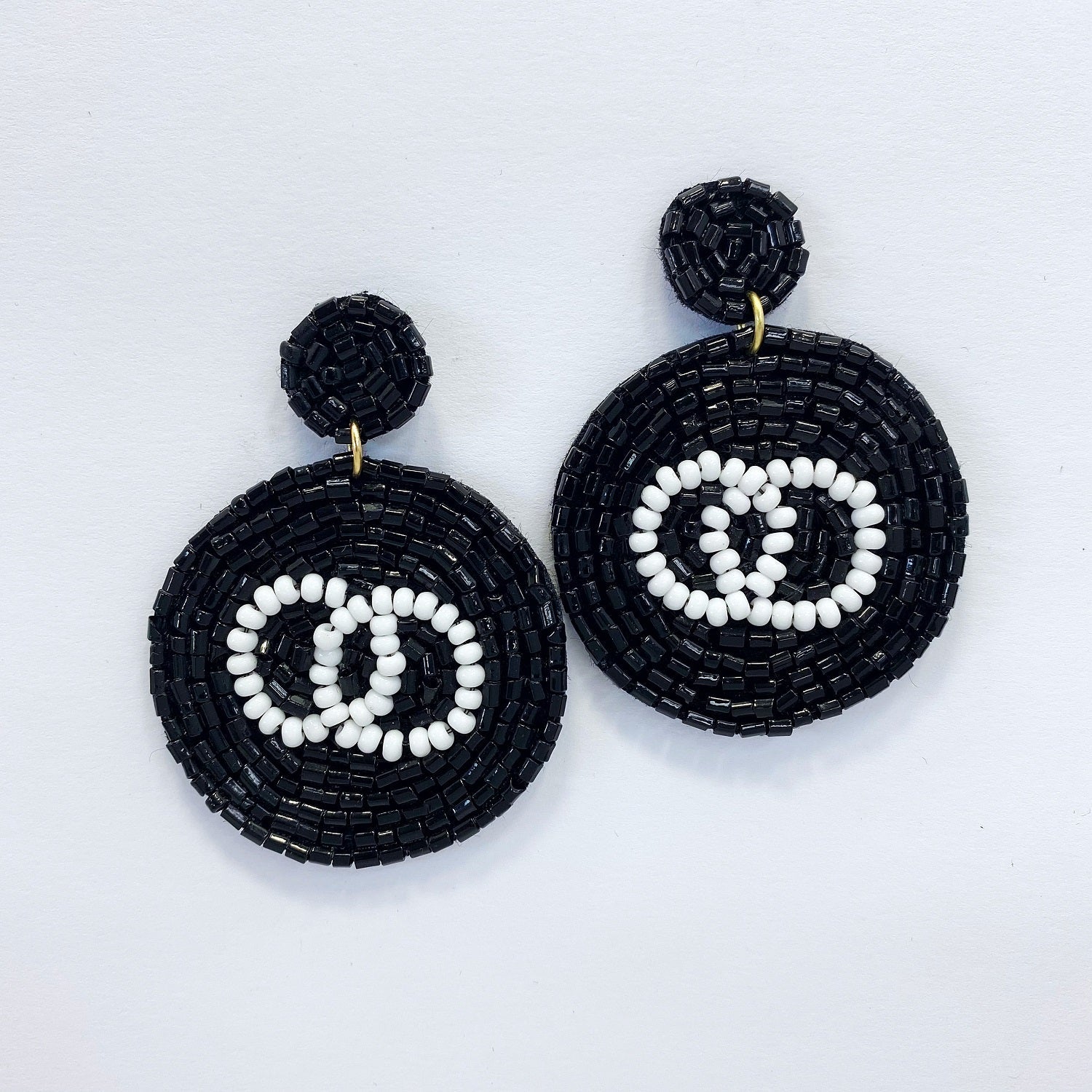 A pair of black and white circle-shaped bead earrings with a dangle post and drop design, displayed on a mannequin head.