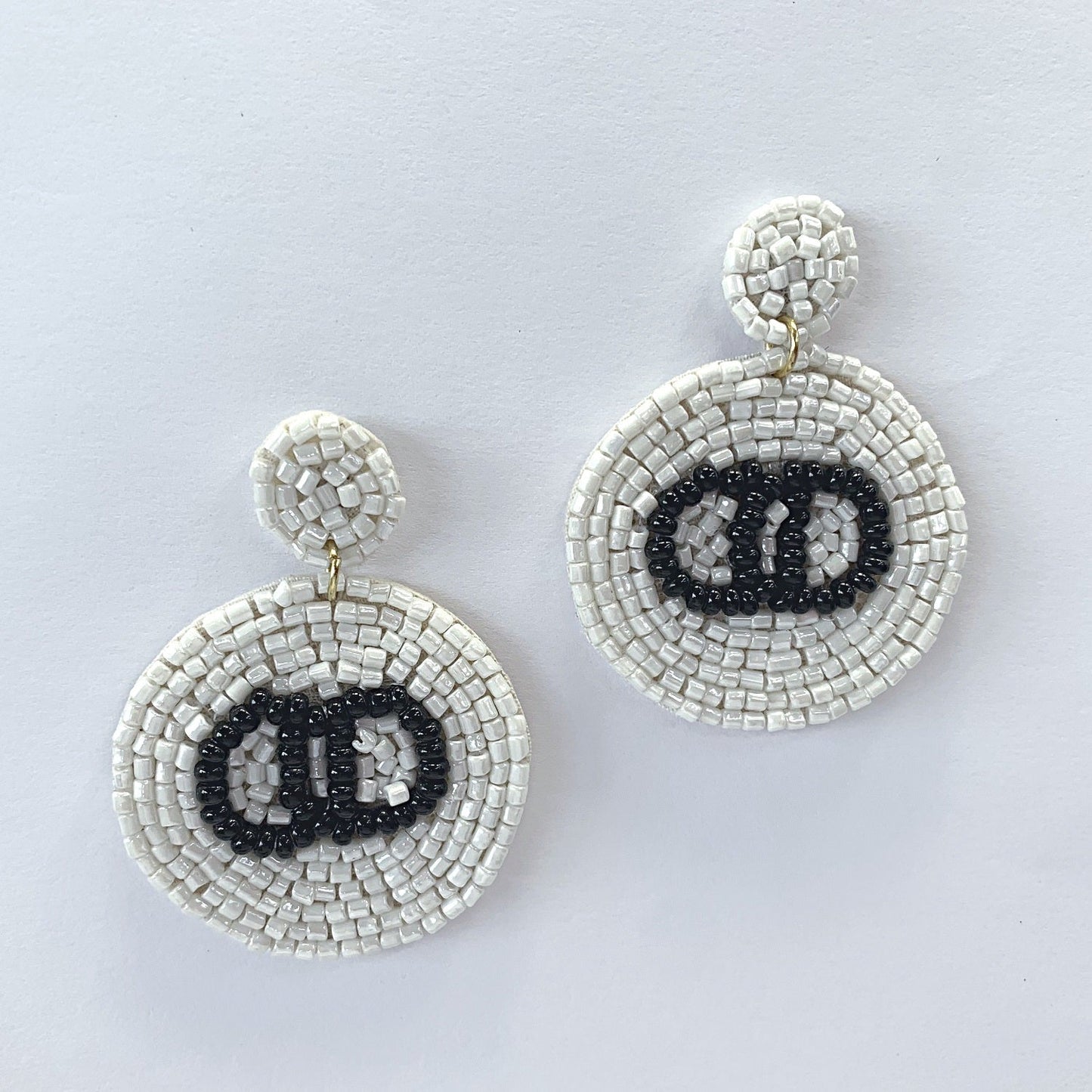 A pair of black and white circle-shaped bead earrings with a dangle post and drop design, displayed on a mannequin head.