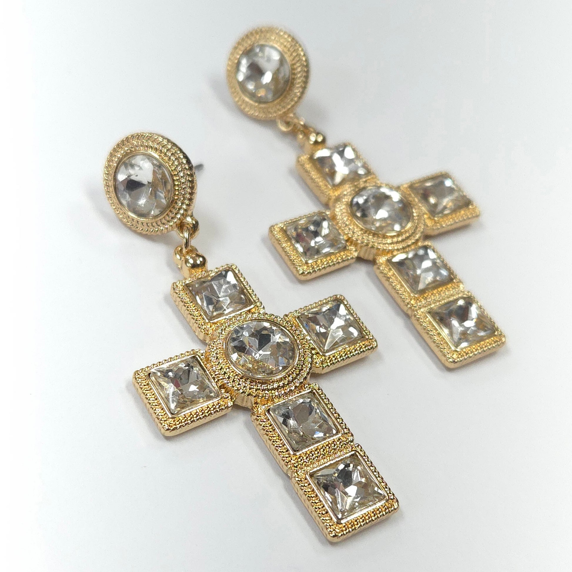 Gold cross-shaped earrings with clear gemstones on a white background