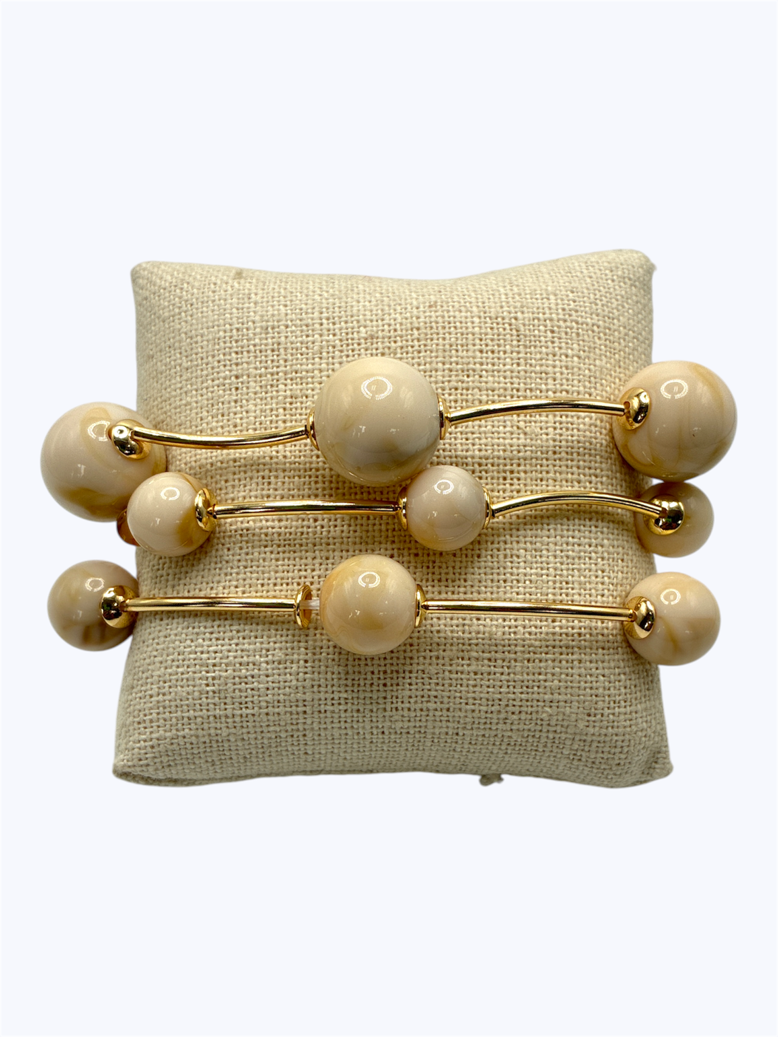 Elegant beaded stretch bracelet set with glossy round beads and gold-tone curved bar accents displayed on linen cushion for boutique fashion accessories collection