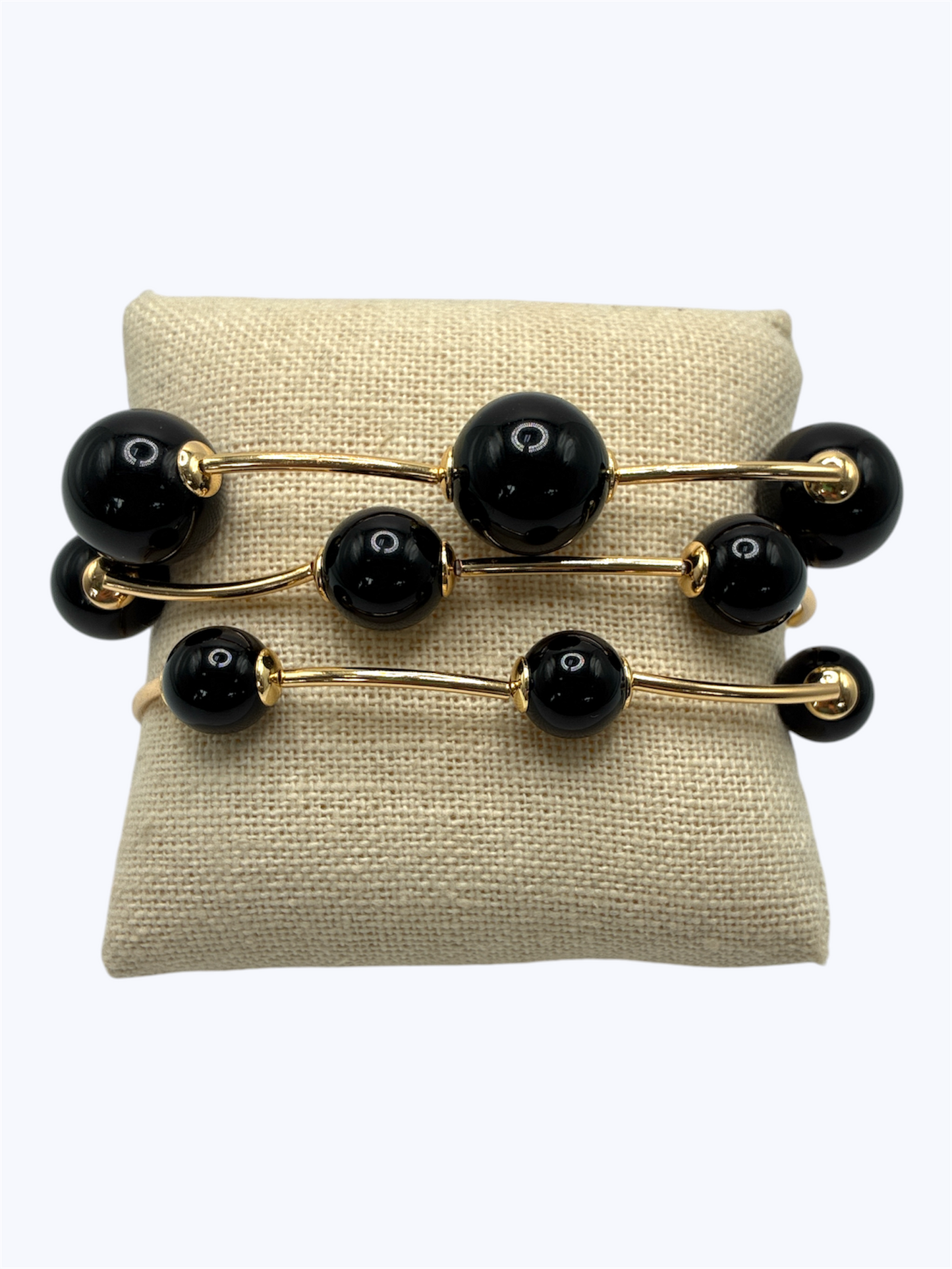 Elegant beaded stretch bracelet set with glossy round beads and gold-tone curved bar accents displayed on linen cushion for boutique fashion accessories collection
