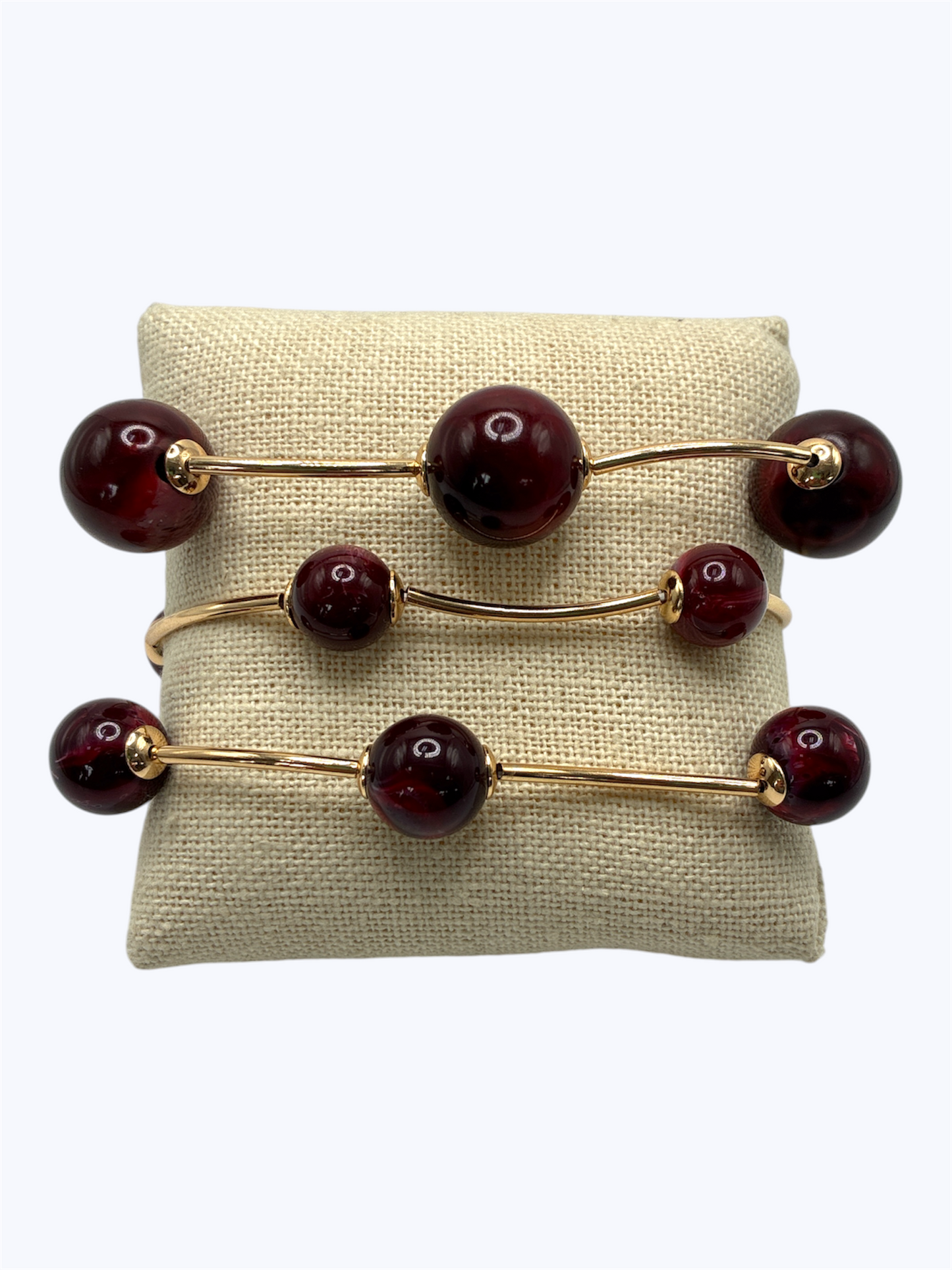 Elegant beaded stretch bracelet set with glossy round beads and gold-tone curved bar accents displayed on linen cushion for boutique fashion accessories collection