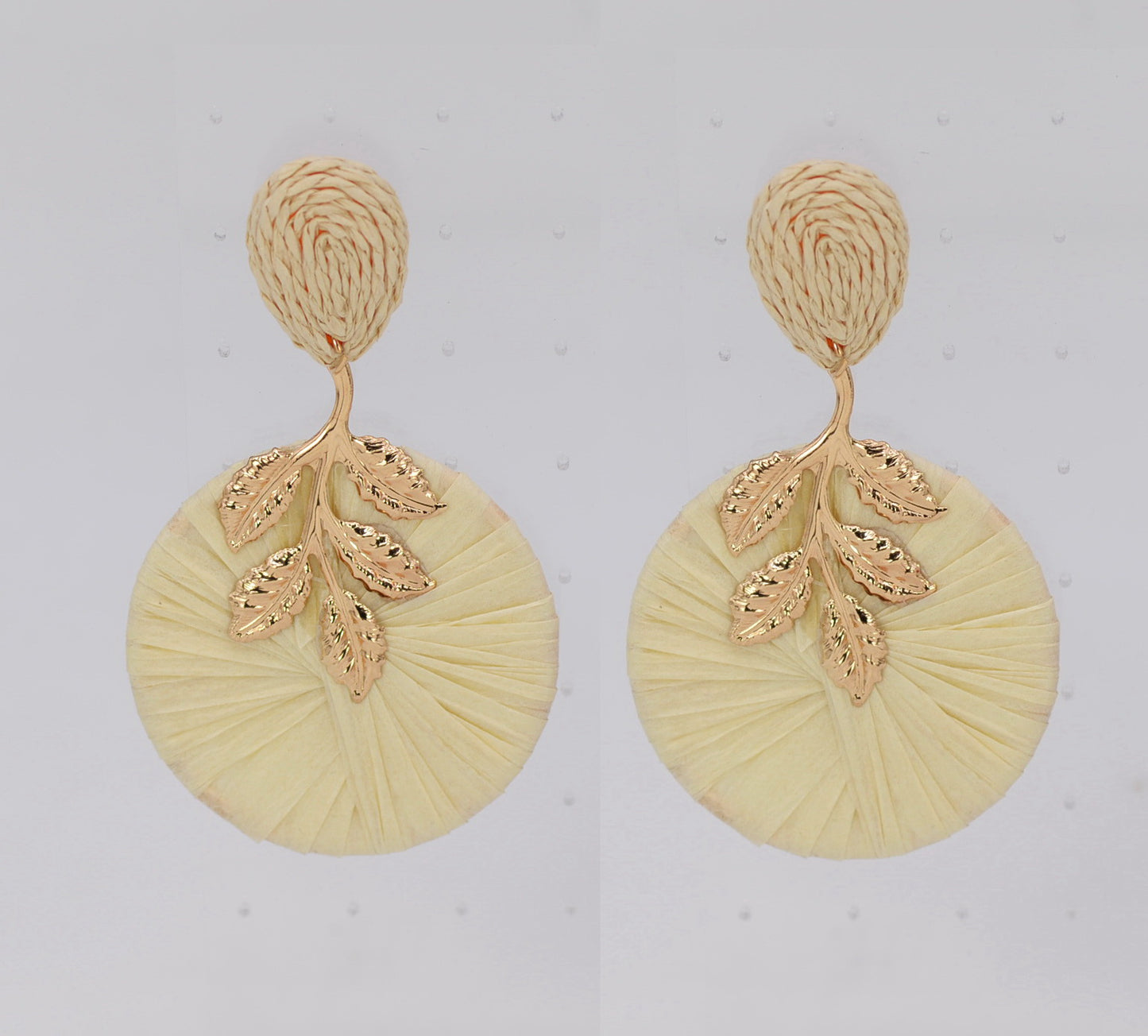Oversized raffia disc drop earrings featuring woven circular detailing with gold tone leaf accents and textured stud tops.