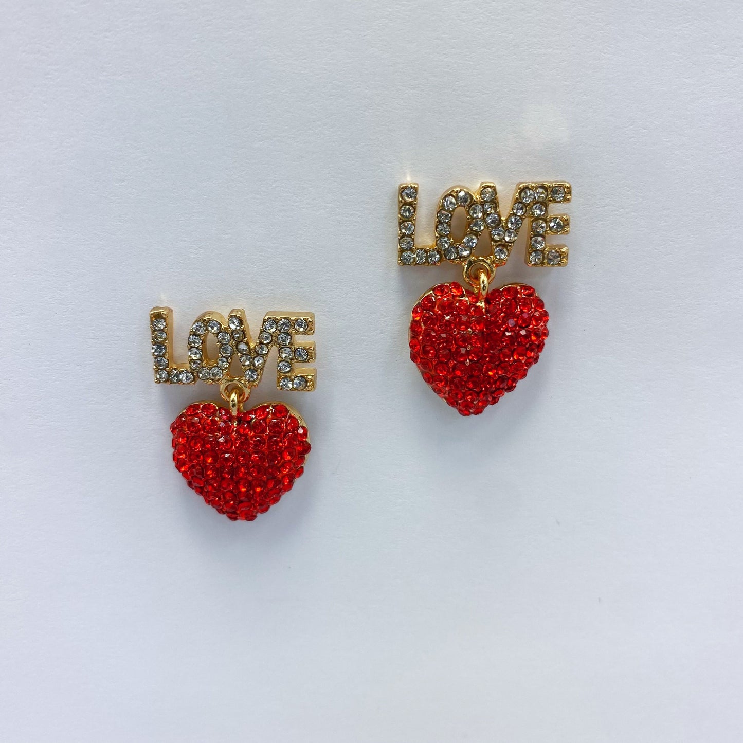 A set of red heart-shaped earrings with the word 'LOVE' written in rhinestones, displayed on a mannequin head from different angles.