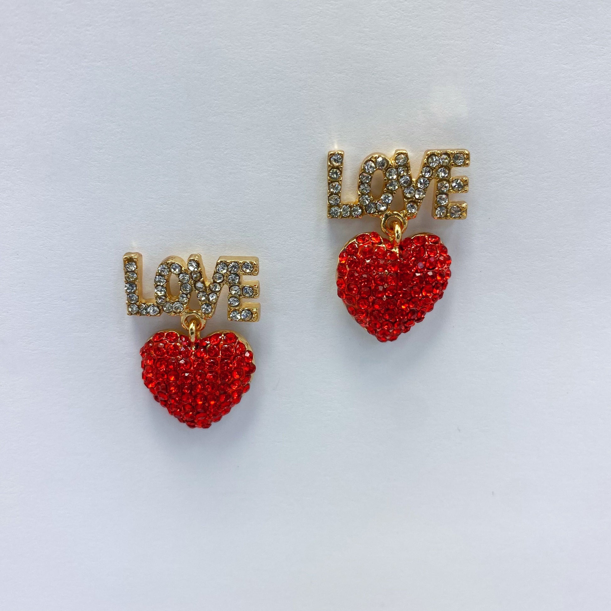 A set of red heart-shaped earrings with the word 'LOVE' written in rhinestones, displayed on a mannequin head from different angles.