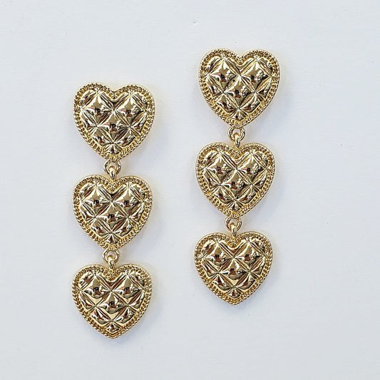 A set of heart-shaped link drop dangle earrings in gold tone, displayed on a mannequin head.