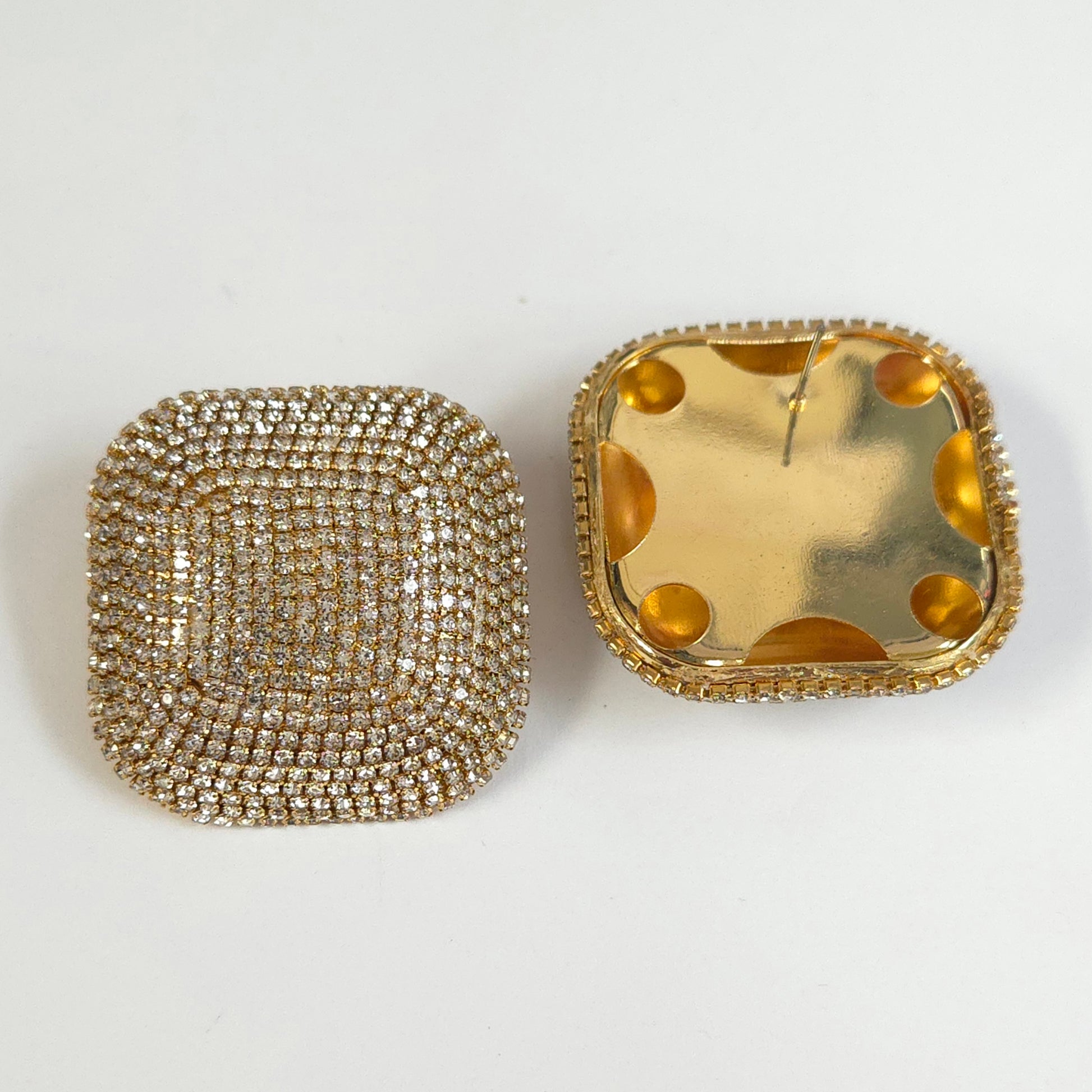 Two square-shaped jewelry items, one with a diamond-studded design and the other with gold polka dot pattern, on a white background.