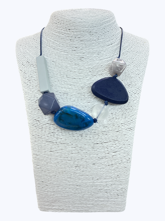 Blue geometric statement necklace with oversized mixed-shape beads and contemporary asymmetrical cord design on mannequin bust