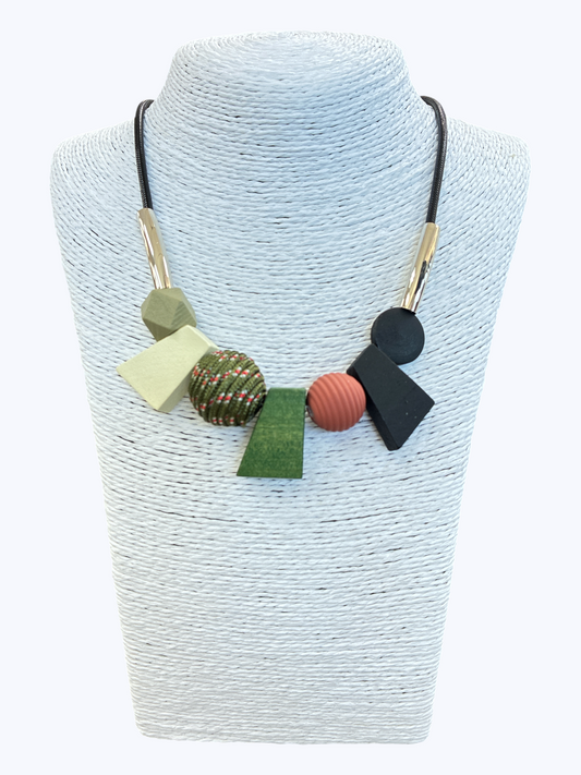 Abstract geometric statement necklace with earthy green, black, and blush accents, textured bead details, and gold-tone tubing for a modern boutique-inspired look.