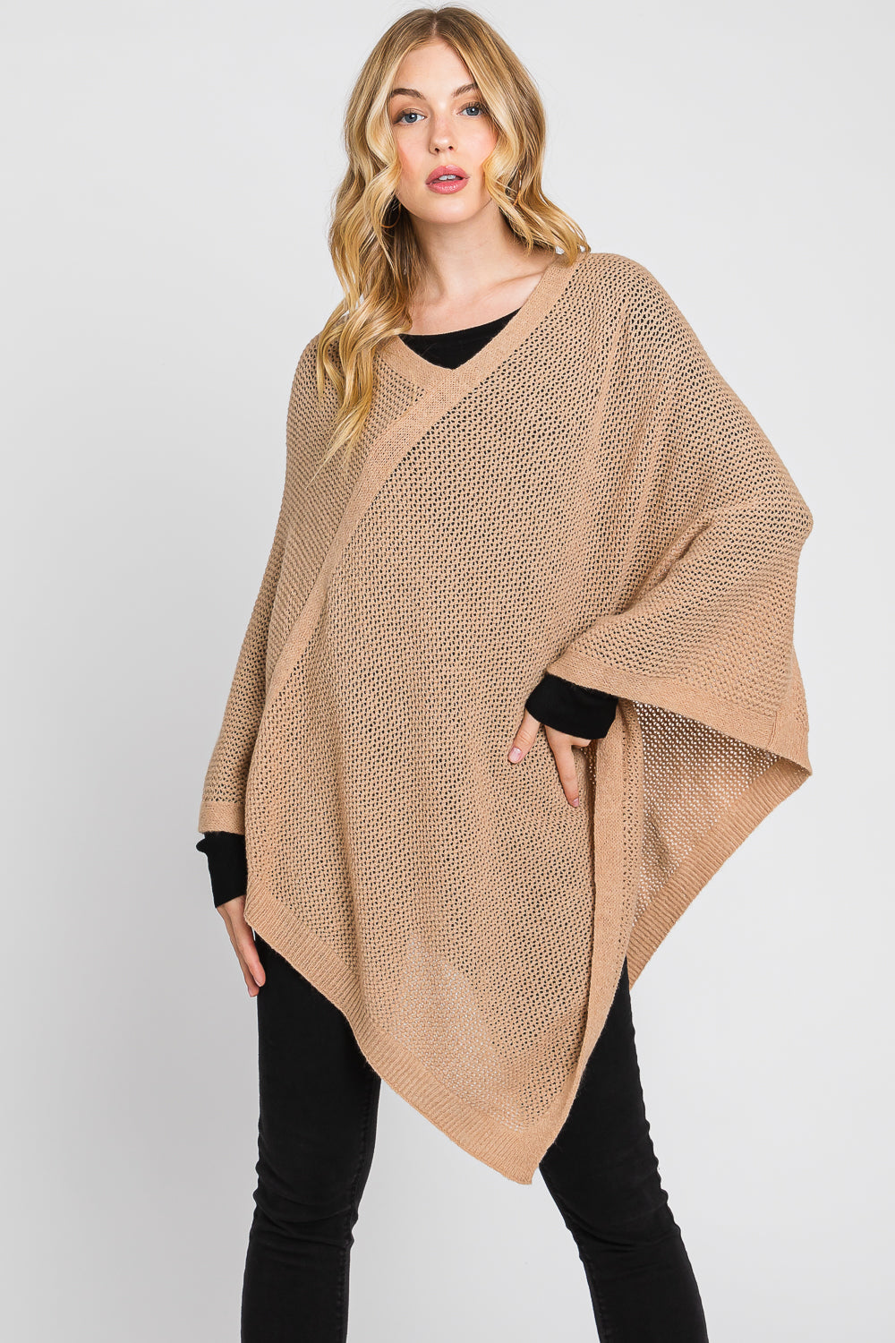 Woman wearing a beige poncho over a black top and pants on a white background