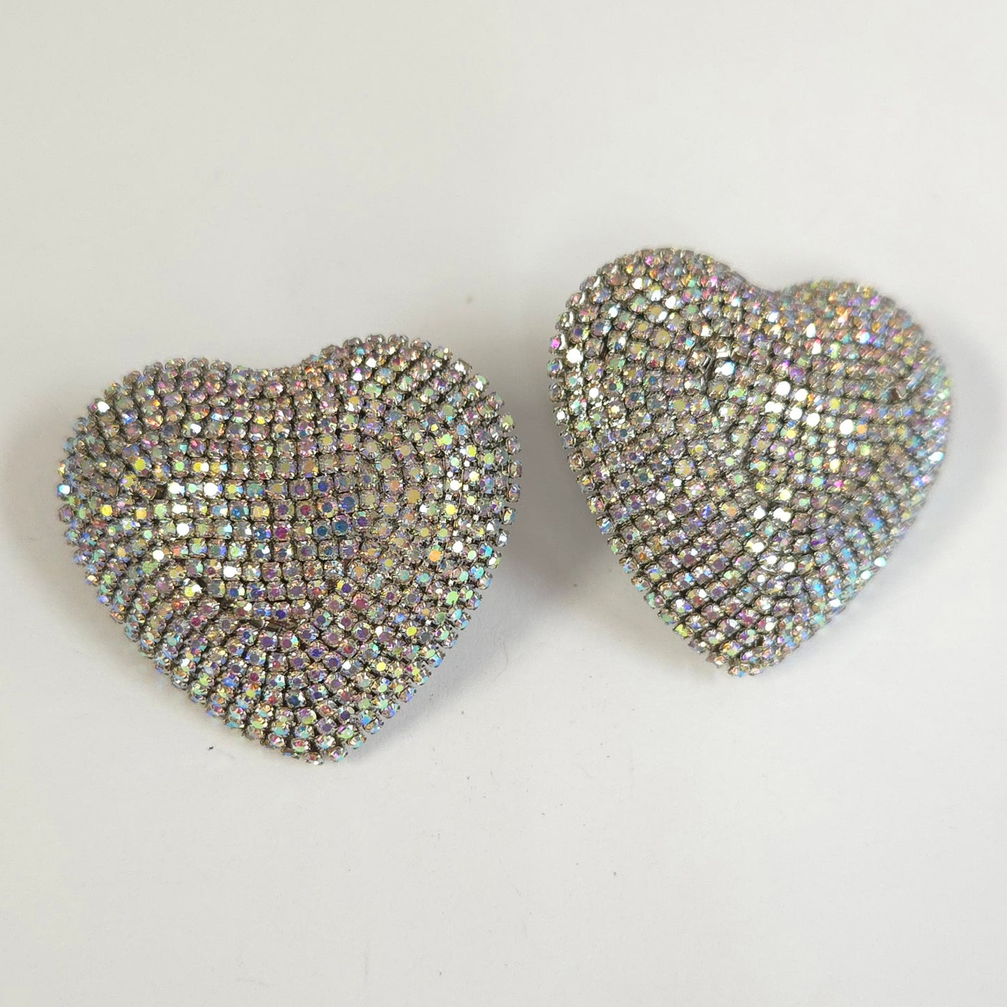 Two heart-shaped earrings with rhinestone embellishments on a light gray background