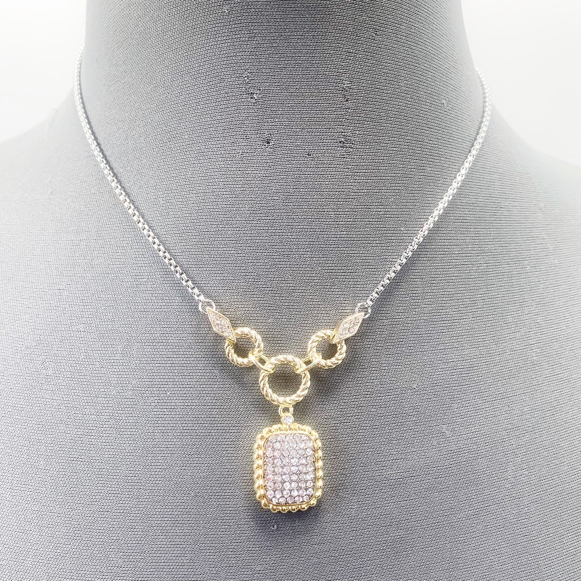 A vintage necklace with a gold-tone frame and clear crystal pendant, displayed on a mannequin.