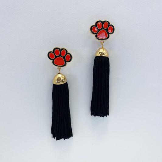A pair of drop dangle post earrings featuring a red animal paw design with a black tassel.
