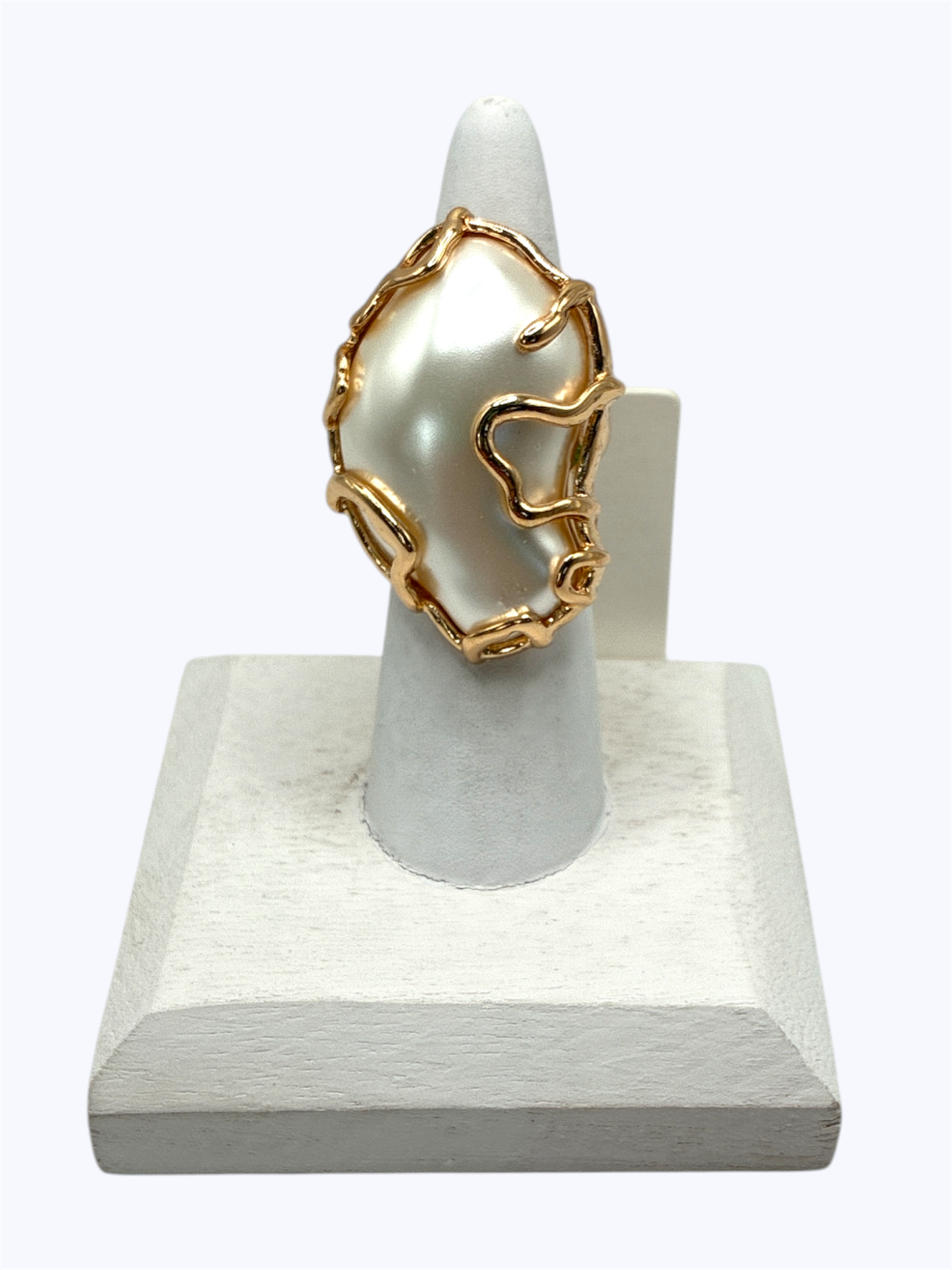 Abstract molten gold-tone statement ring with organic sculptural frame and pearl centerpiece displayed on jewelry cone stand for modern boutique fashion accessories collection