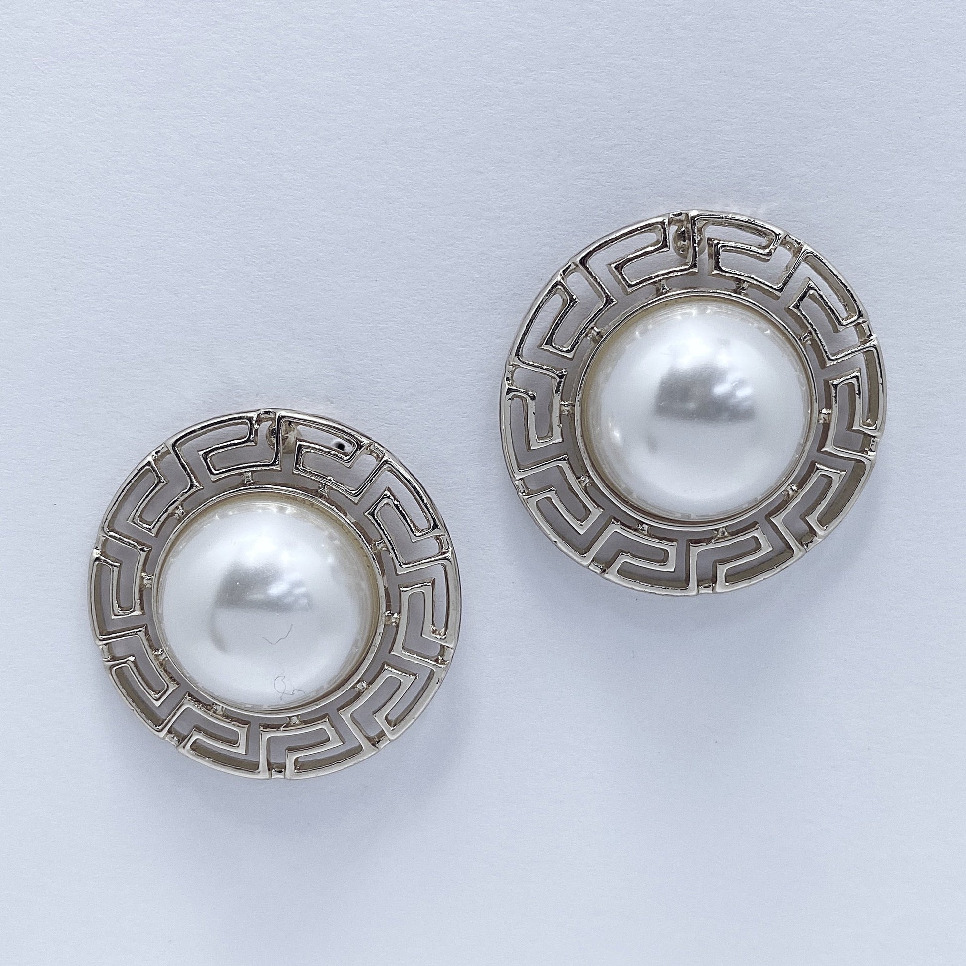 A pair of earrings with a pearl centered on a white background