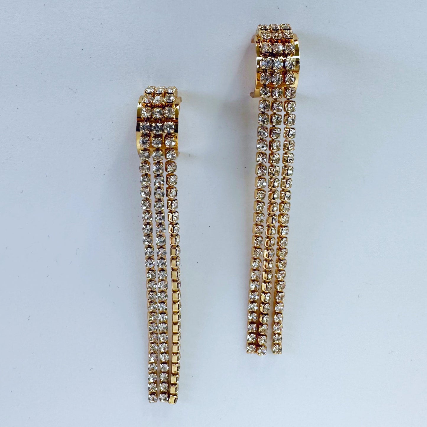 A pair of gold-colored rhinestone-studded earrings with a geometric pattern, displayed on a mannequin head.
