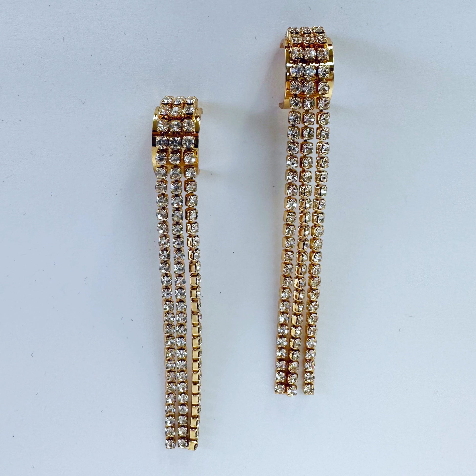 A pair of gold-colored rhinestone-studded earrings with a geometric pattern, displayed on a mannequin head.