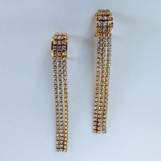 A pair of gold-colored rhinestone-studded earrings with a geometric pattern, displayed on a mannequin head.