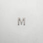 Silver letter 'M' charm on a light gray background