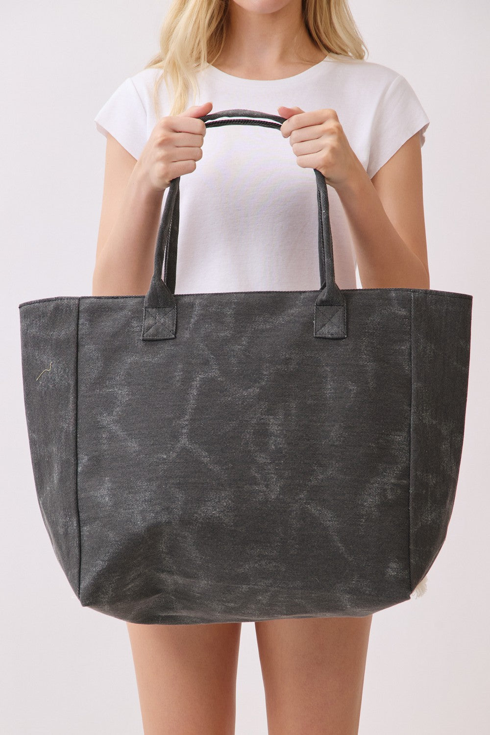 Person holding a dark gray tote bag against a white background