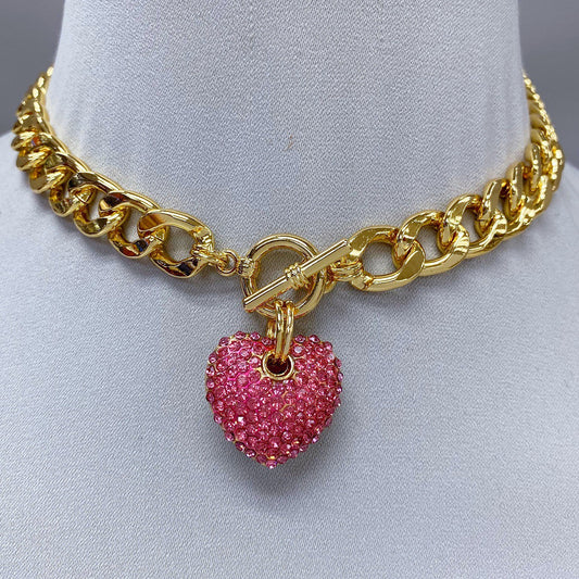 Gold chain necklace with a pink heart charm on a mannequin.