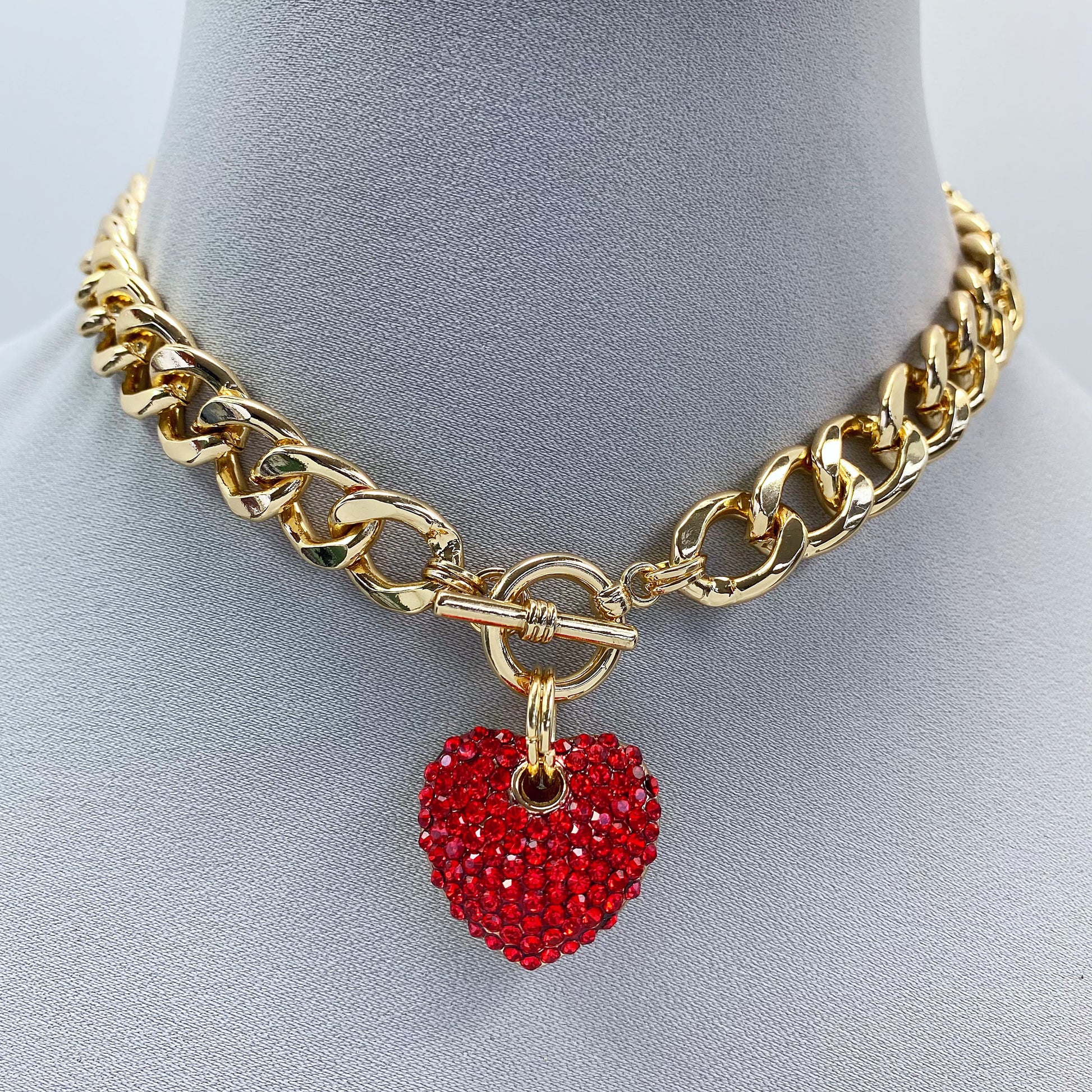 Gold chain necklace with a red heart pendant on a mannequin bust.