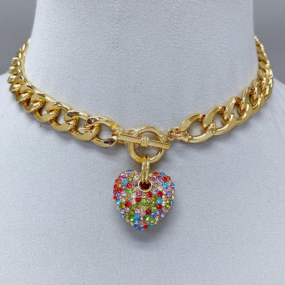 Gold chain necklace with a colorful heart-shaped pendant on a mannequin bust.