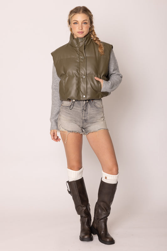 Woman wearing a green vest, gray shirt, denim shorts, and black knee-high boots on a white background