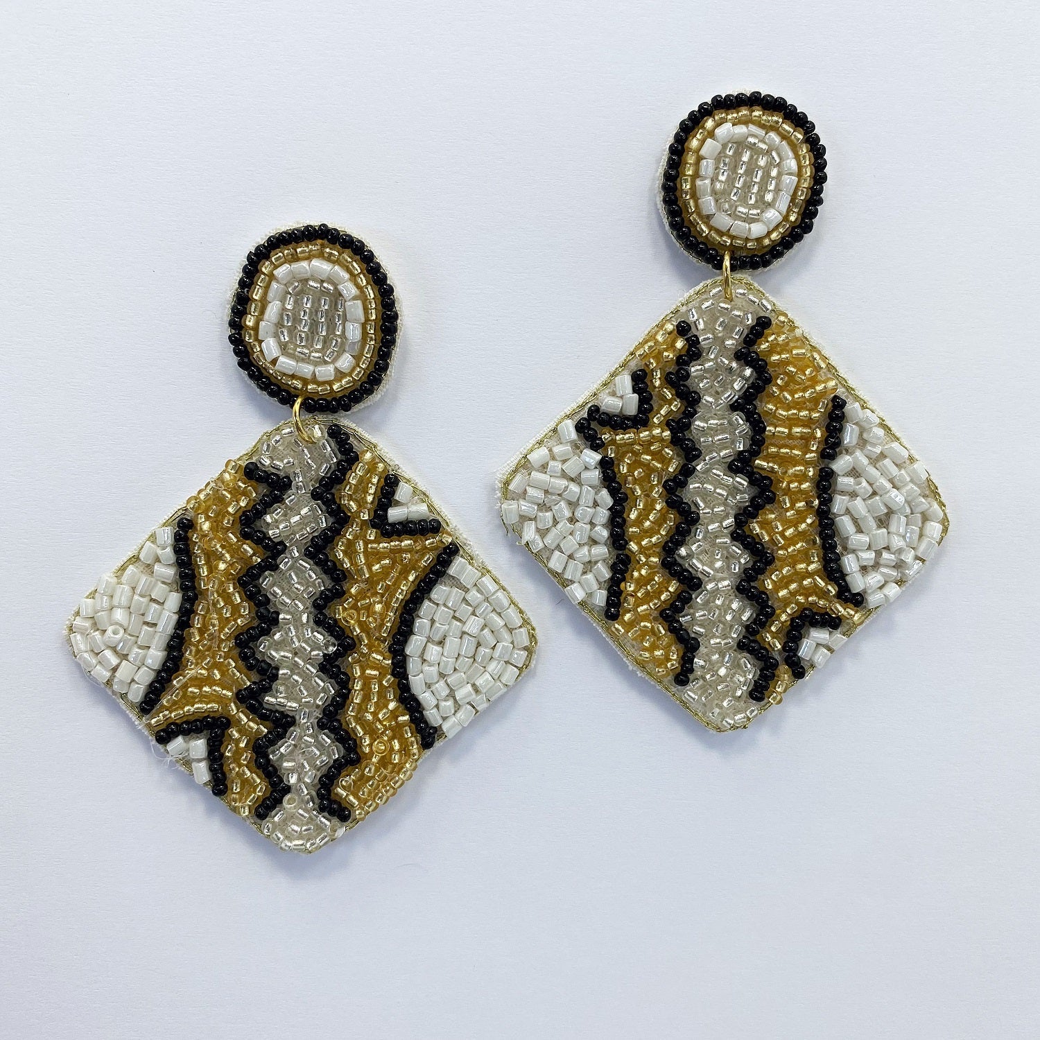 A gold,black and white earrings on a white background