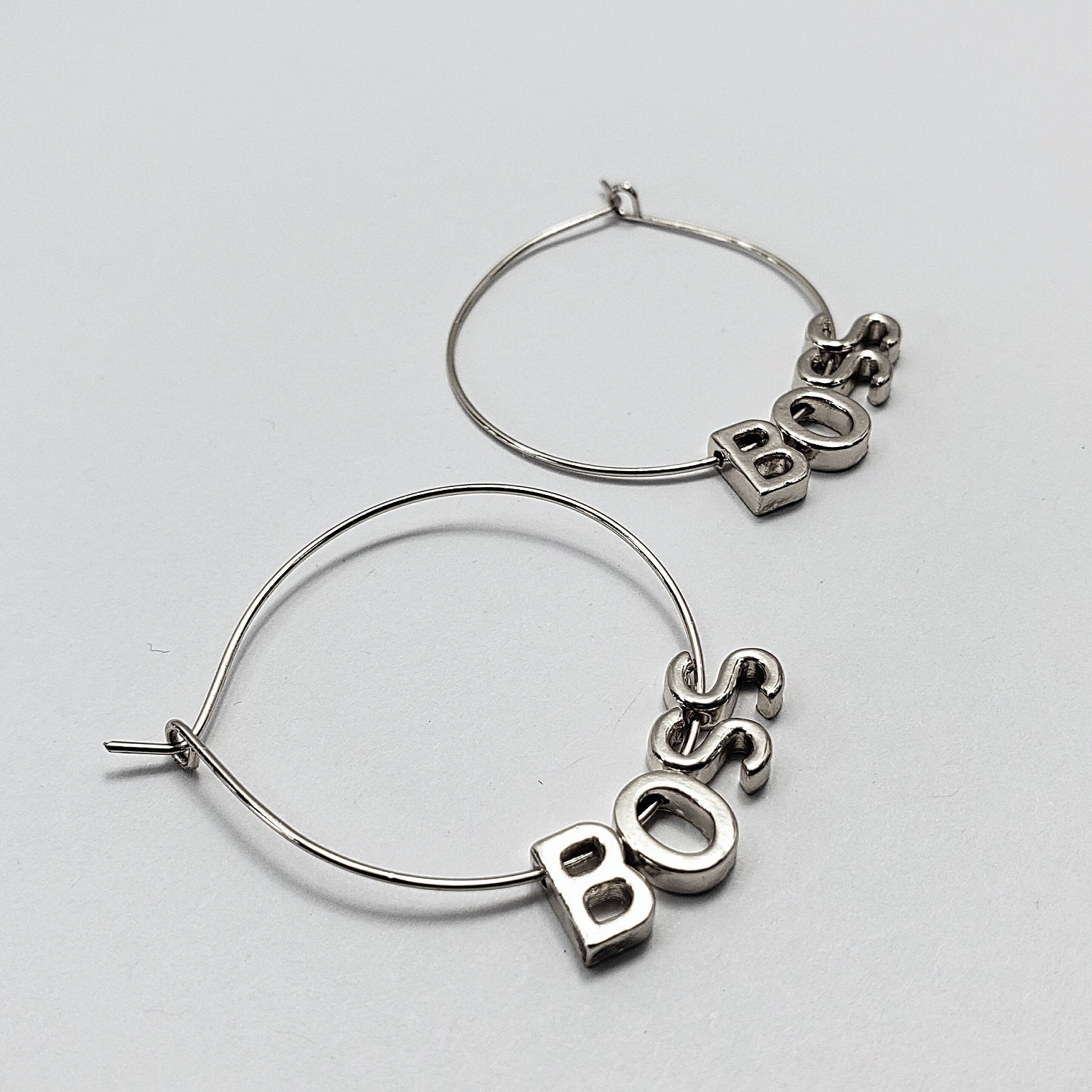 A pair of silver-colored hoop earrings with the word 'BOSS' written in a retro font, displayed in three different views on a white background.