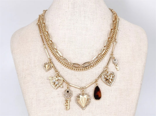 Gold necklace with heart and key charms on a mannequin bust against a white background